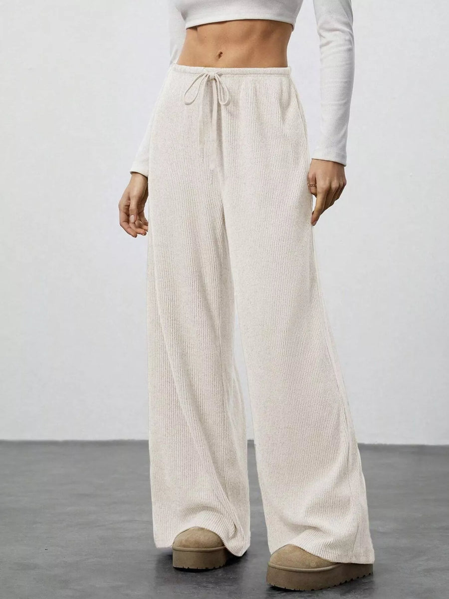 Person wearing beige wide-leg pants and white top on a plain background
