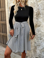 Woman wearing a black long-sleeve top and striped skirt against a stone wall.