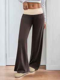 Person wearing brown wide-leg pants and a light-colored top against a white wall.