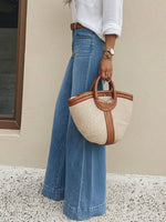 Person holding a straw handbag with brown handles wearing blue jeans and a white shirt.