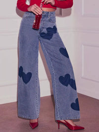 Person wearing blue jeans with heart patterns and a red top, standing against a white wall.