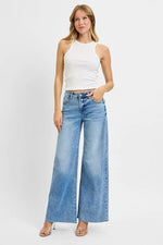 Woman wearing a white sleeveless top and blue wide-leg jeans on a white background