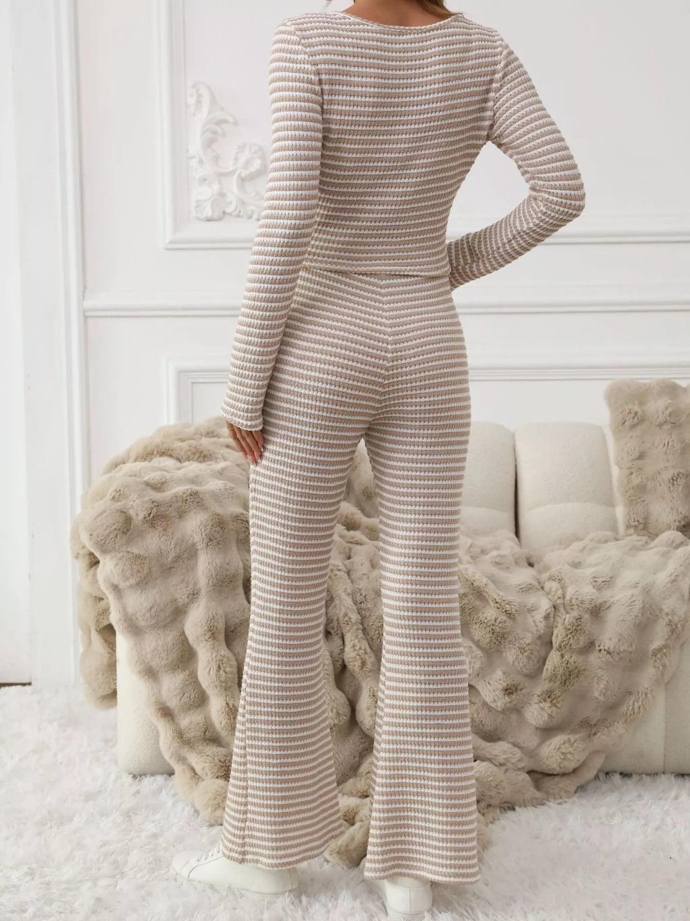 Person wearing a beige ribbed jumpsuit in a cozy room with white walls and textured pillows.
