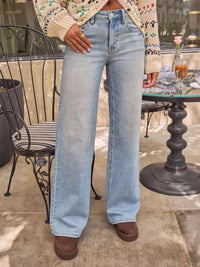 Person wearing light blue jeans standing outdoors near a table with a plant and drink.