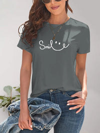 Person wearing a gray t-shirt with 'Smile' text, holding a denim jacket against a neutral background