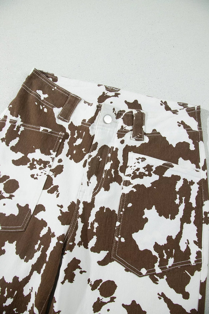 Close-up of a pair of pants with a brown and white abstract splatter pattern, showing the waistband, belt loops, button, and front pockets.