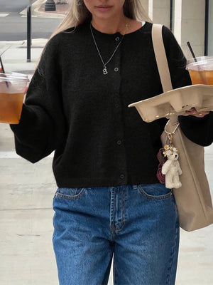 Person wearing a black sweater and blue jeans, holding drinks and a beige bag with a keychain.