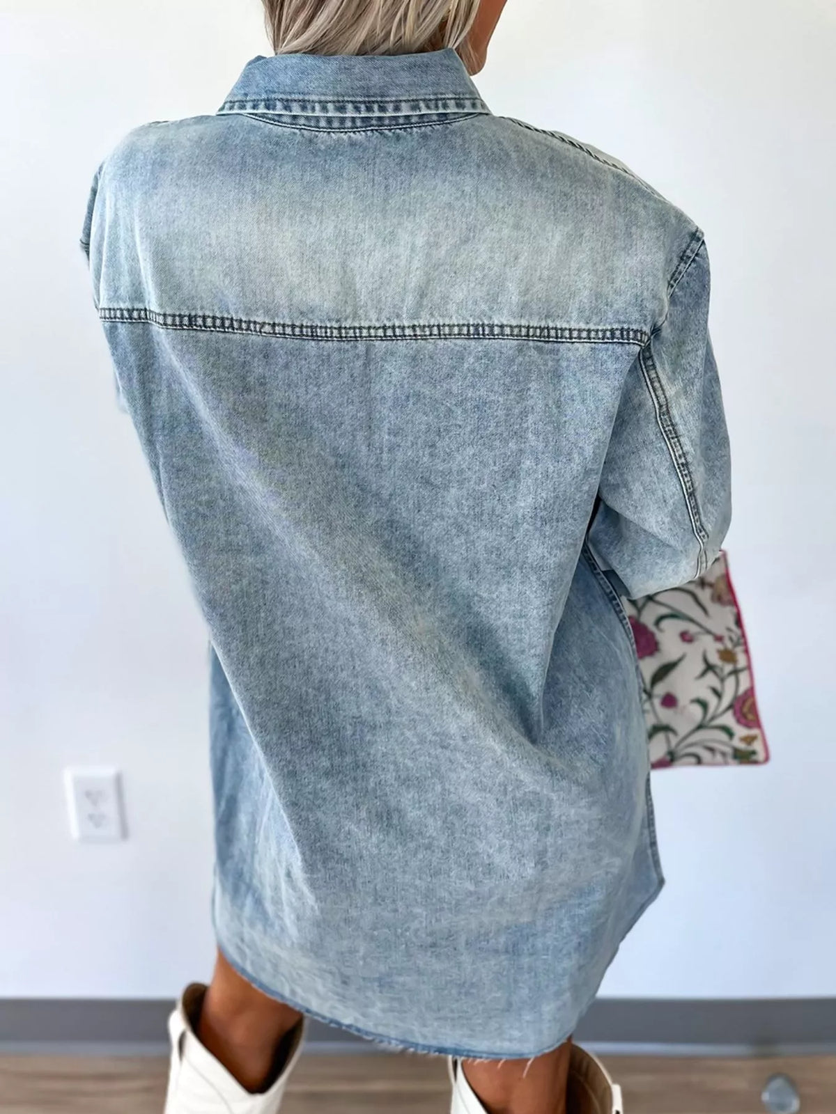 Person wearing a light blue denim shirt with a white wall background