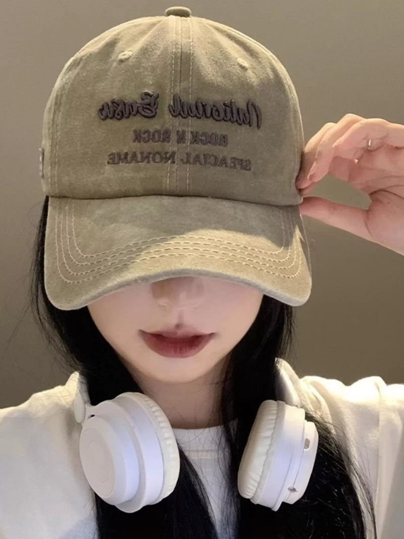 Person wearing a beige cap with text and white headphones, against a neutral background