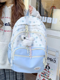Light blue backpack with star pattern held by a person, with a store window in the background.