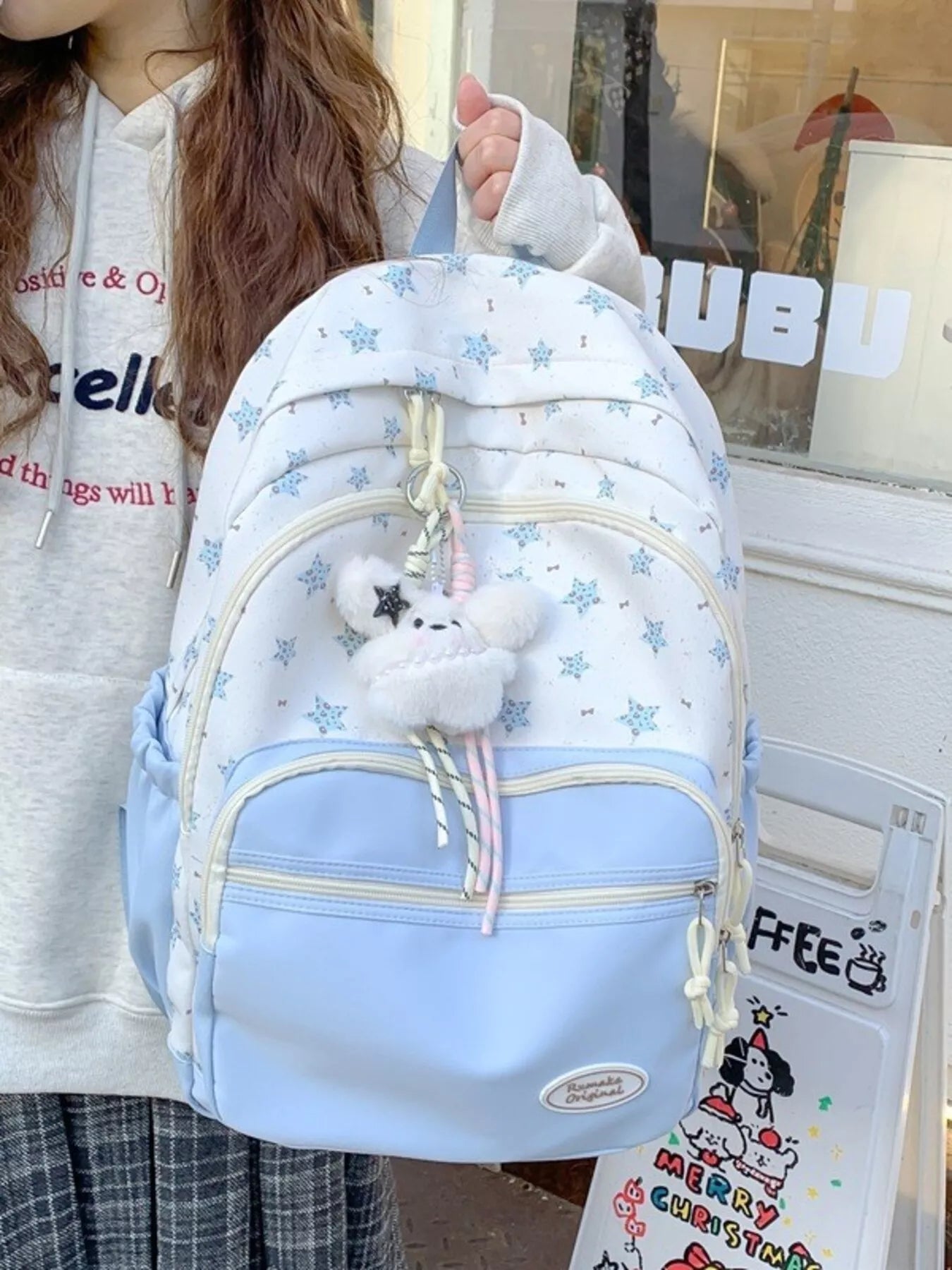 Light blue backpack with star pattern held by a person, with a store window in the background.
