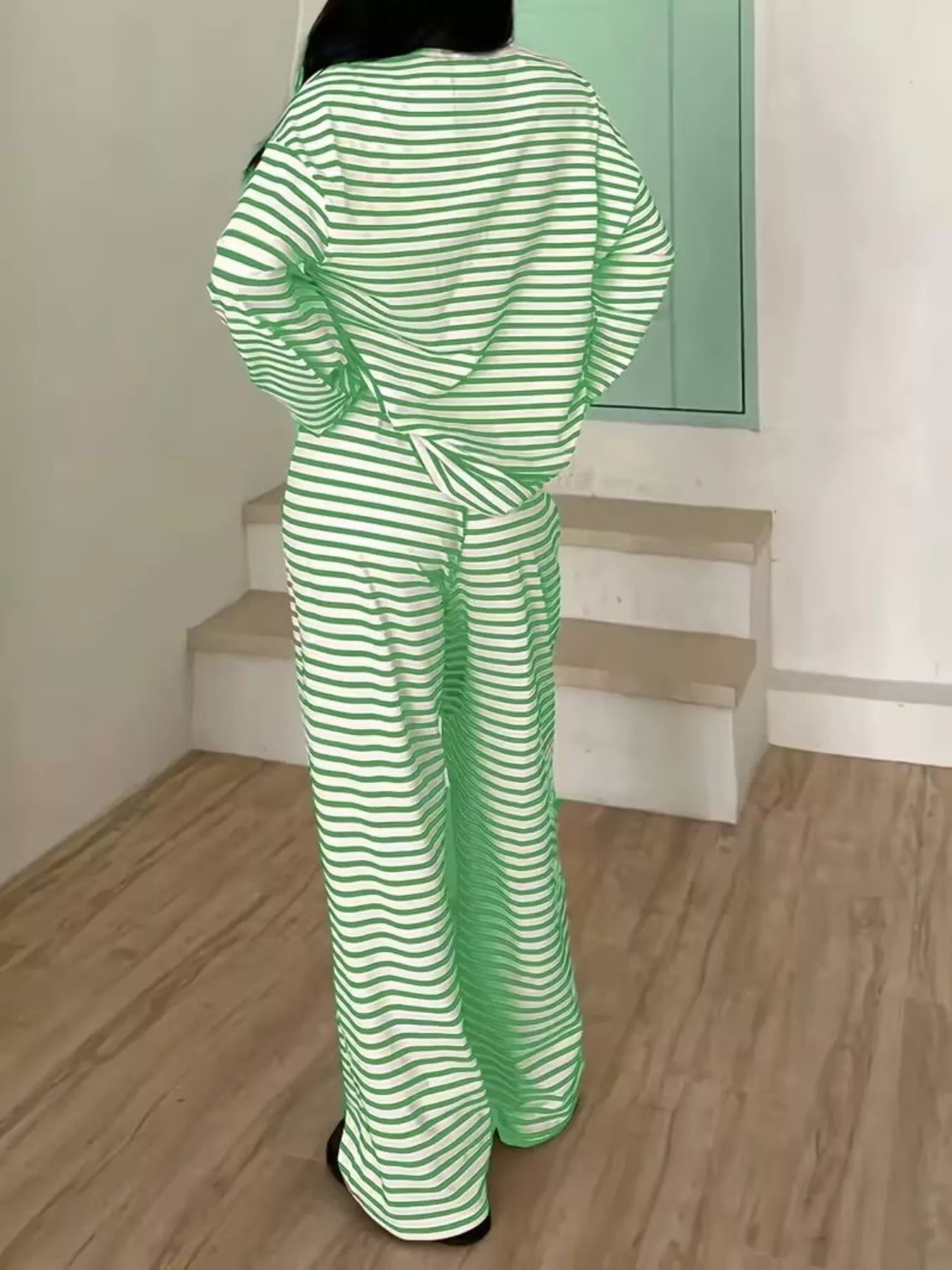 Person wearing a green and white striped outfit standing in a room with wooden floor and staircase.