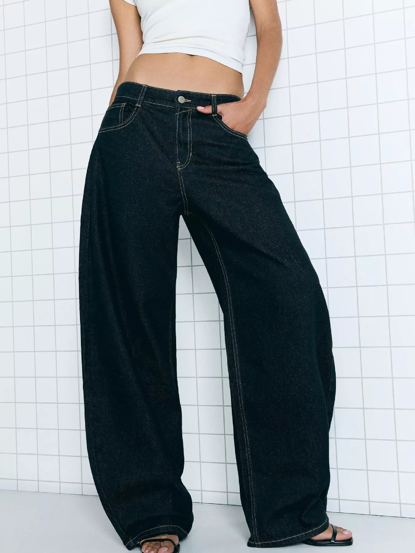 Person wearing wide-leg black jeans against a white grid background