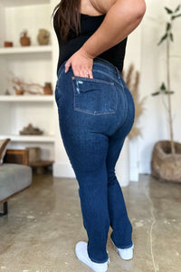 Person wearing blue jeans and a black top in a room with a shelf in the background