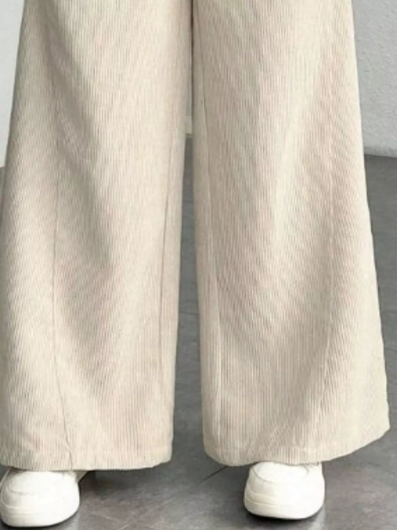 Beige wide-leg pants worn with white shoes on a neutral background