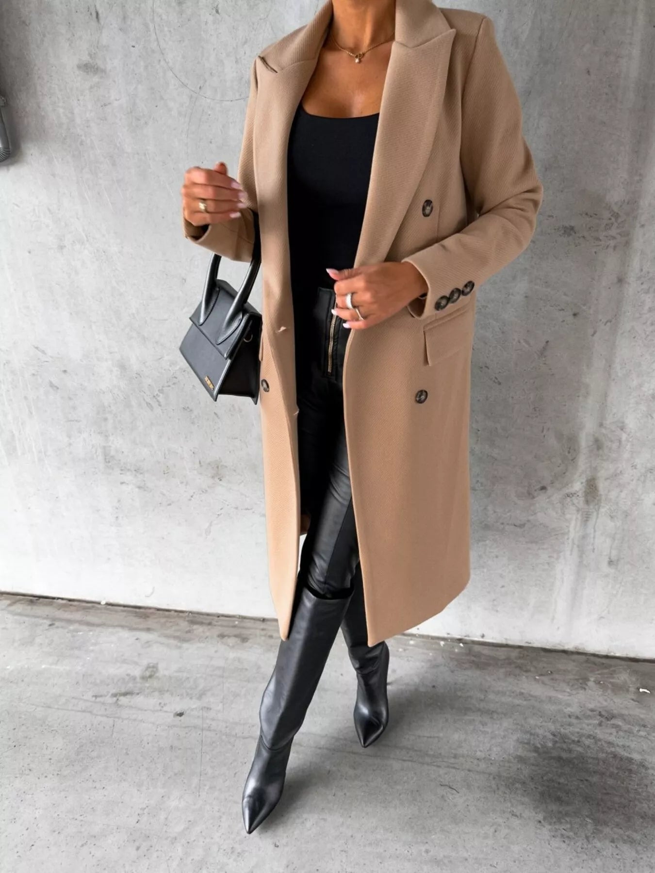 Person wearing a beige coat and black boots against a gray concrete wall.