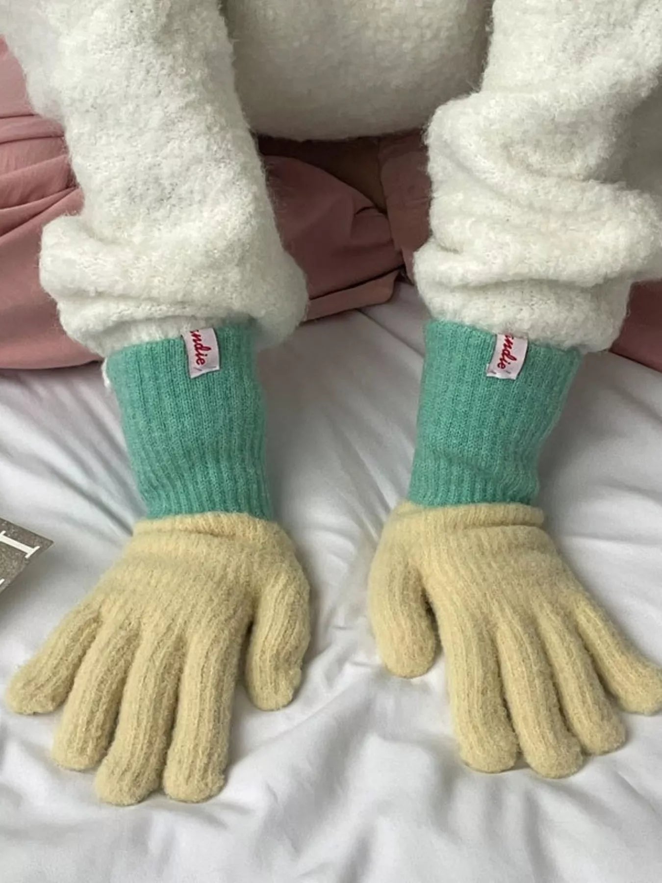 Pair of green and yellow gloves worn by a person with white sleeves.