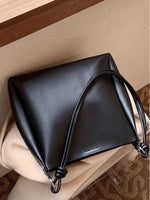 Black leather handbag with a handle on a beige surface