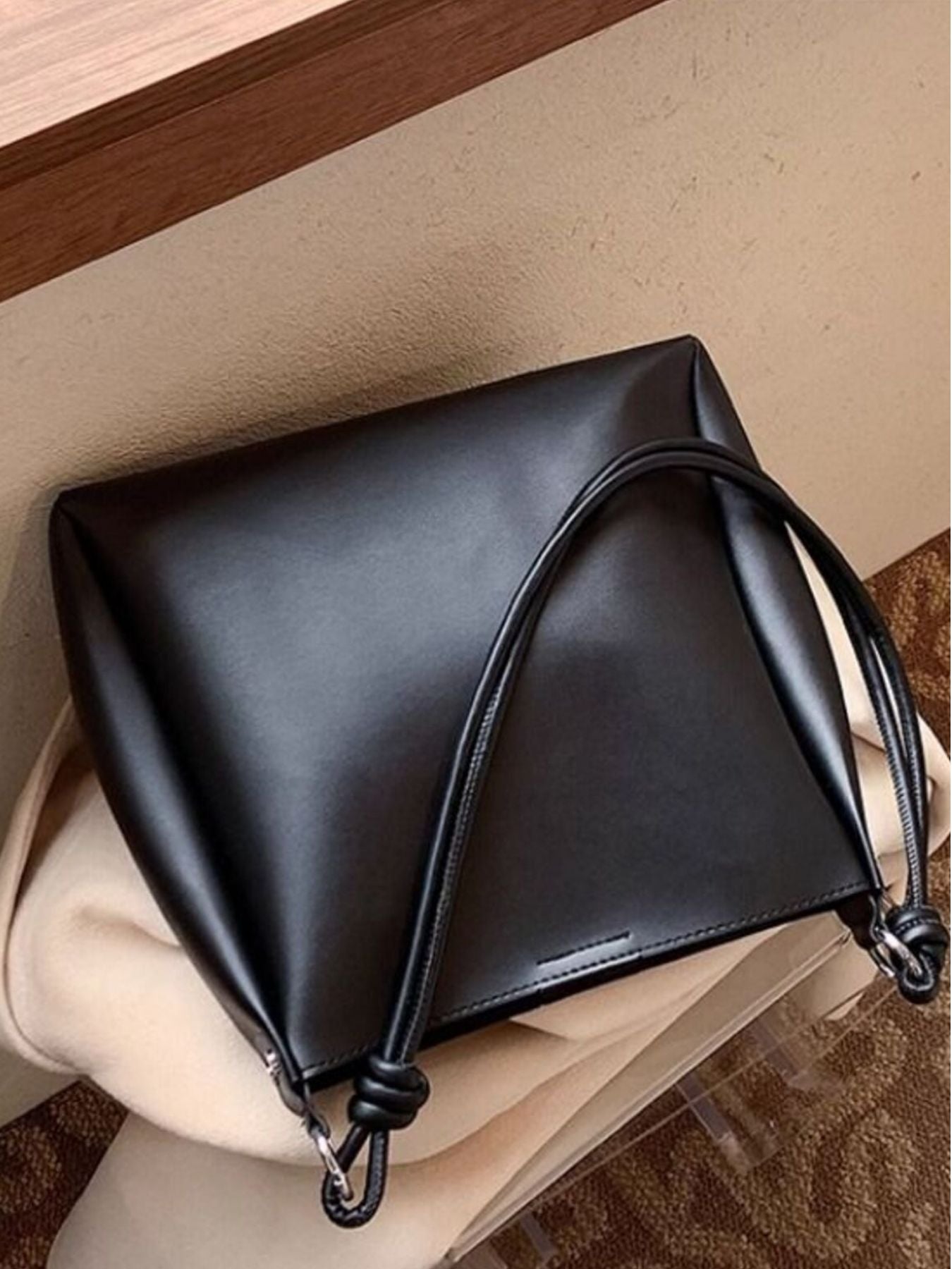 Black leather handbag with a handle on a beige surface