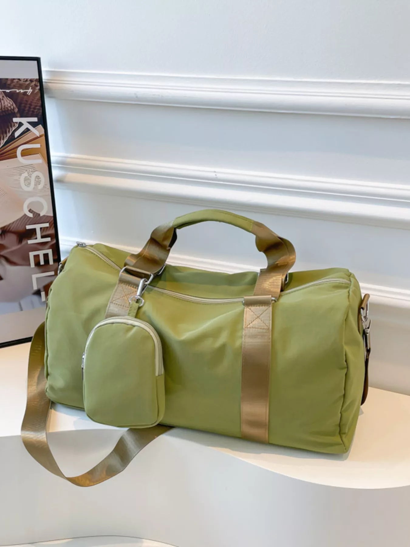 Green duffel bag with gold accents on a white surface