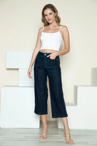 Woman wearing a white top and dark blue jeans standing against a light background