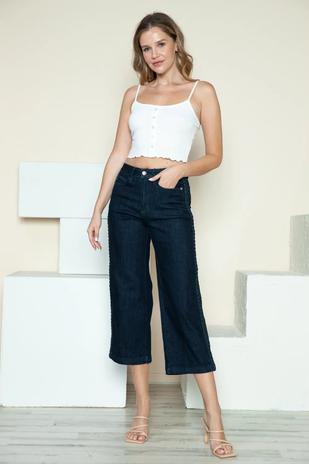Woman wearing a white top and dark blue jeans standing against a light background