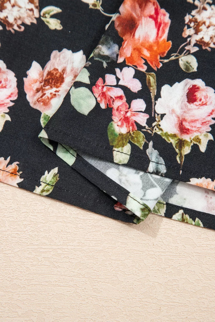 Floral-patterned paper with pink and orange flowers on a black background, placed on a beige surface.
