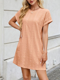 Woman wearing a peach-colored dress with a textured pattern against a light gray wall.