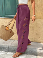 Person wearing purple pants with floral embroidery, standing against a stone wall.