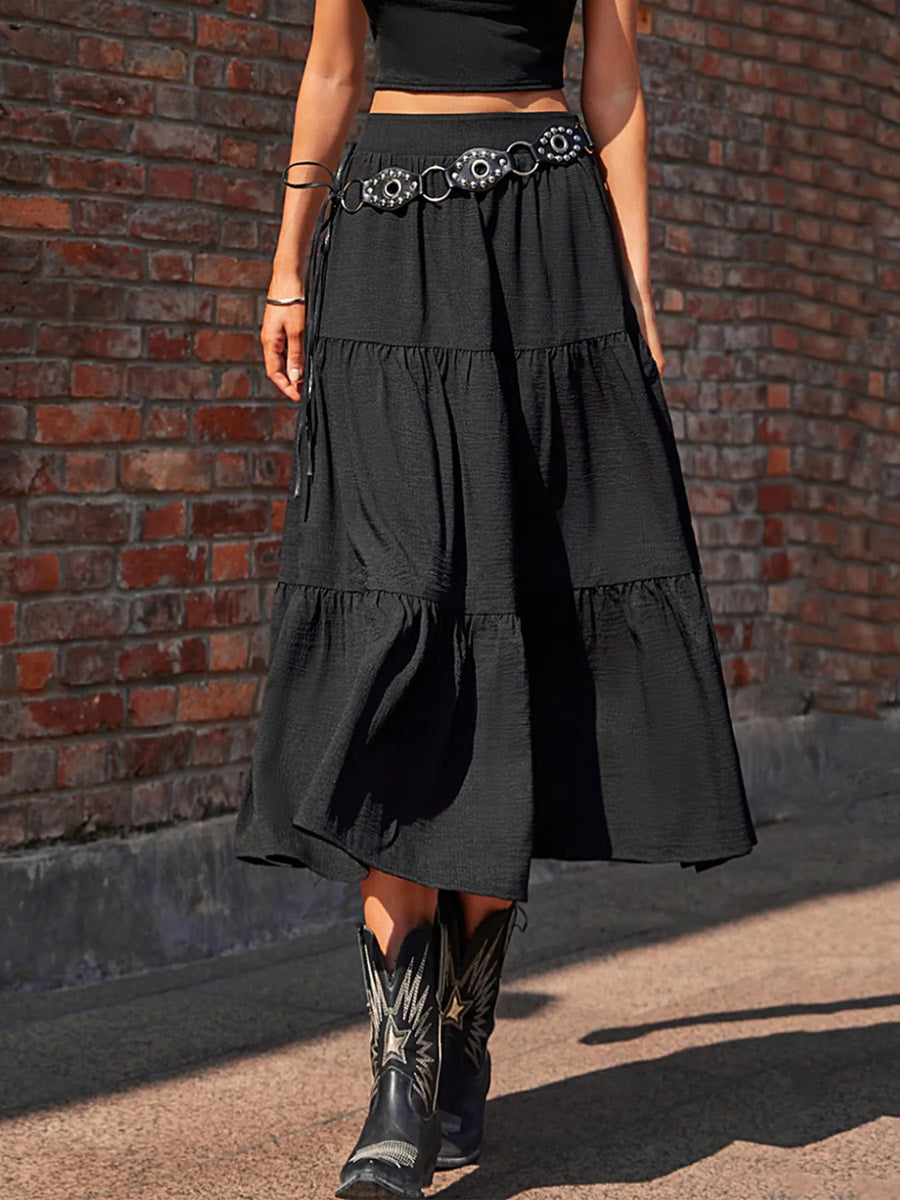 Person wearing a black tiered skirt with a belt and cowboy boots against a brick wall.