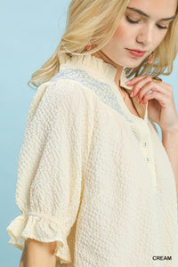 Woman wearing a cream-colored blouse with lace details against a light blue background