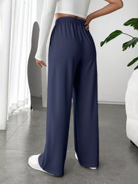 Person wearing navy wide-leg pants with a white top and shoes in a minimalistic room.