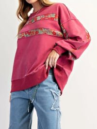 Person wearing a pink sweater with floral embroidery and blue jeans on a white background