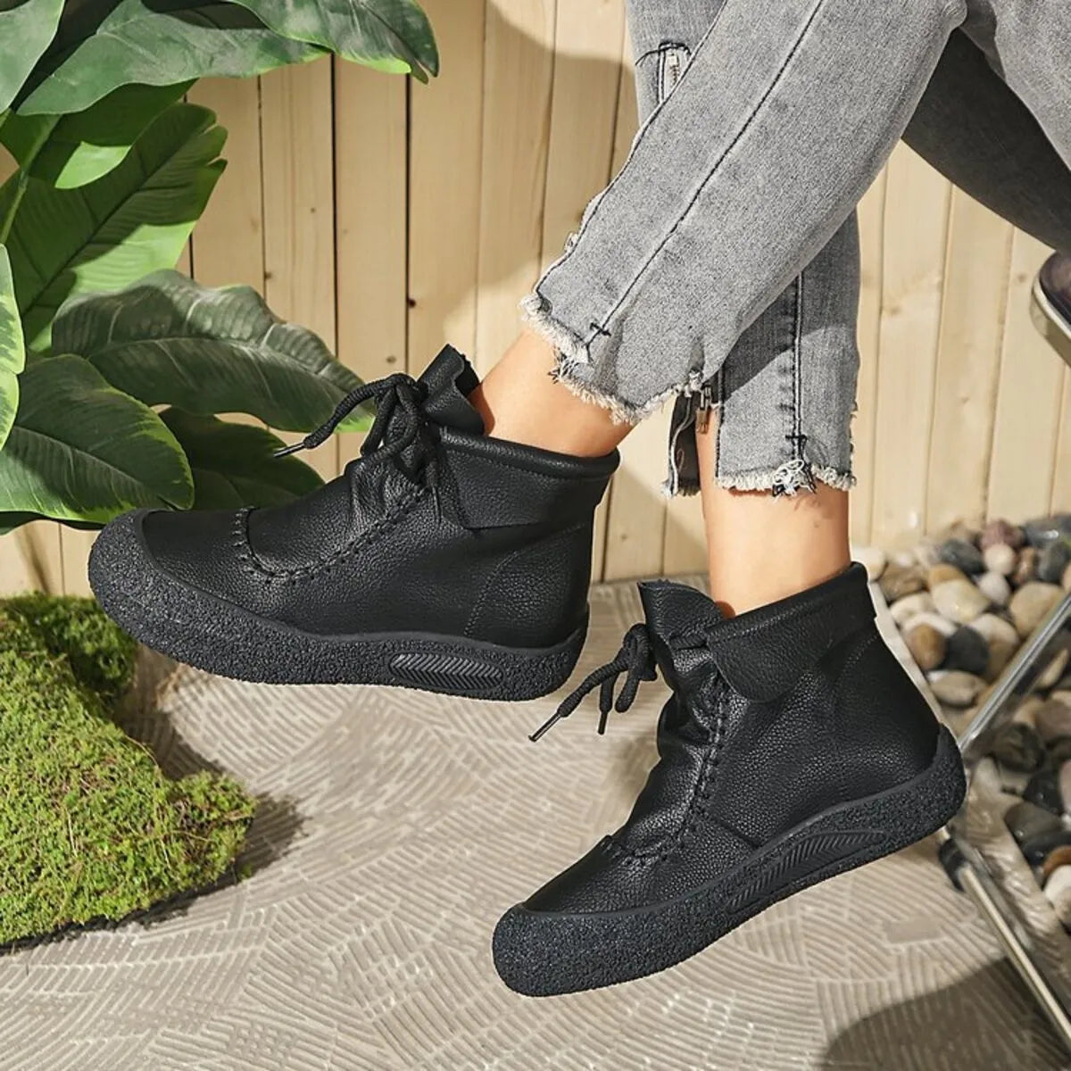 Person wearing black boots with a wooden fence and plant in the background