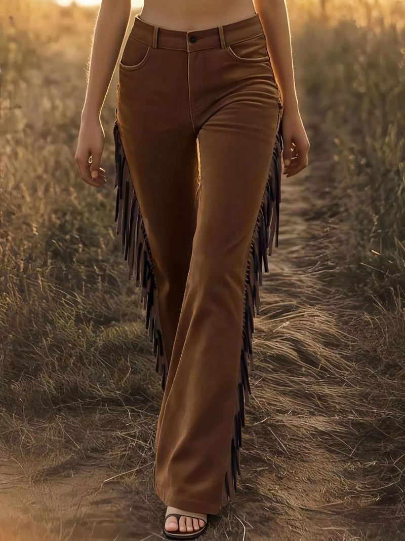 Person wearing brown fringed pants walking through a field at sunset.