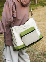 Person holding a beige and green bag outdoors
