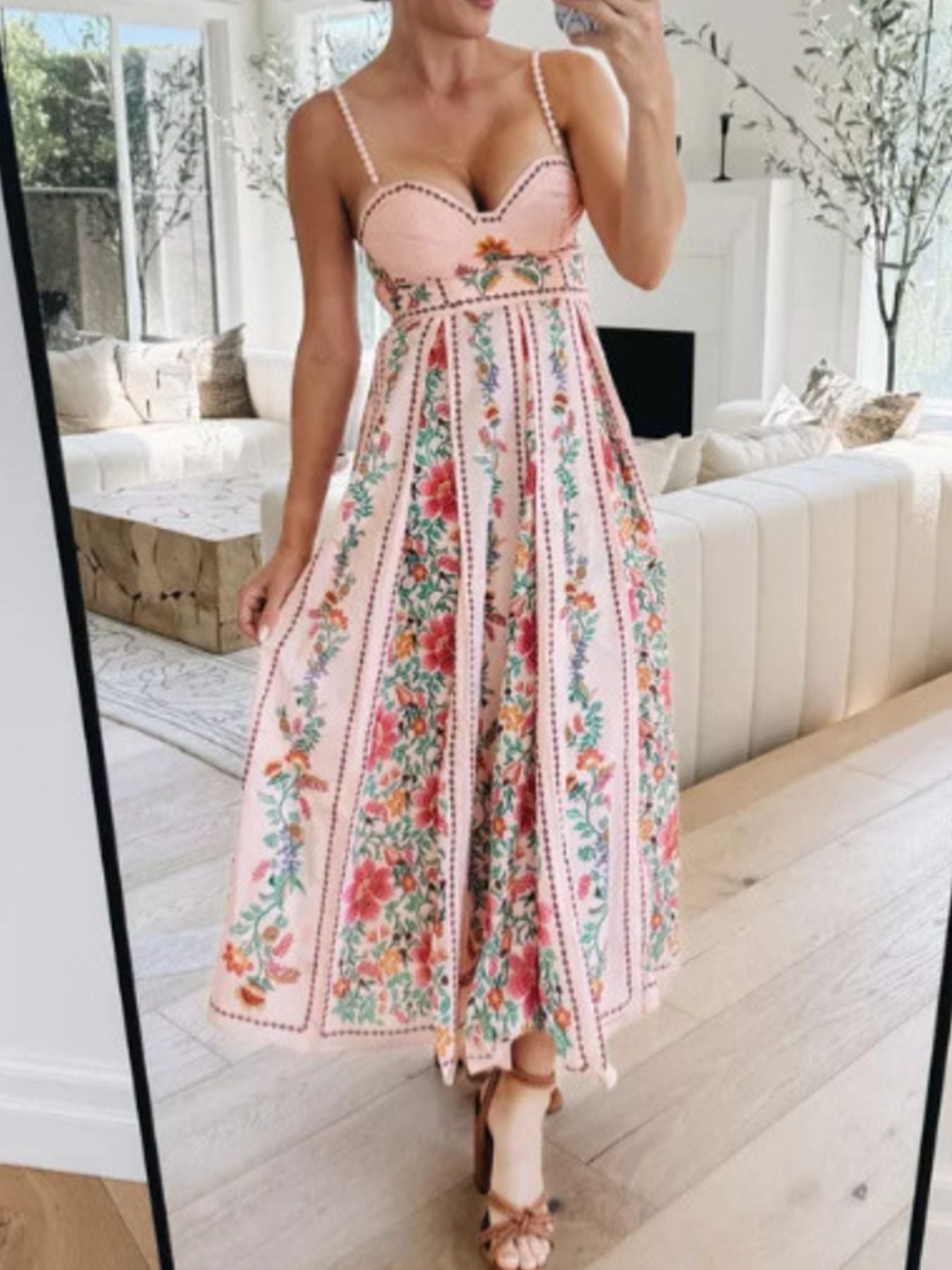 Person wearing a floral dress taking a mirror selfie in a bright living room.