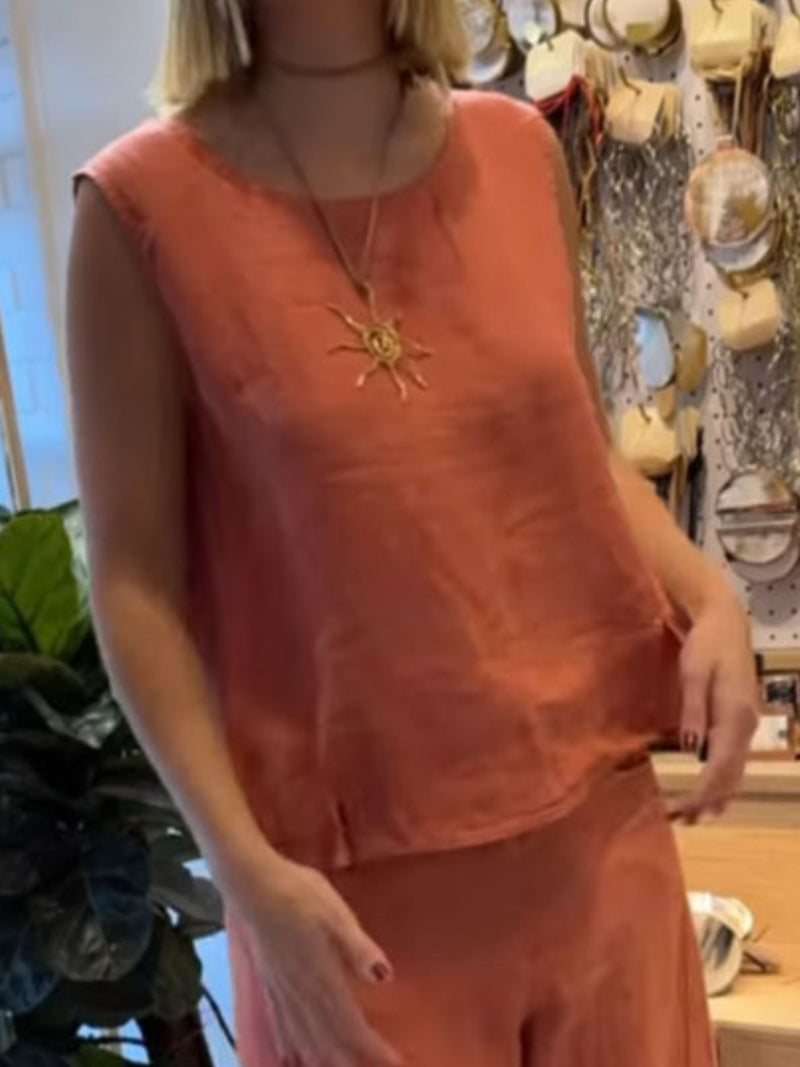 Person wearing a sleeveless orange top with a sun pendant necklace in a store setting.