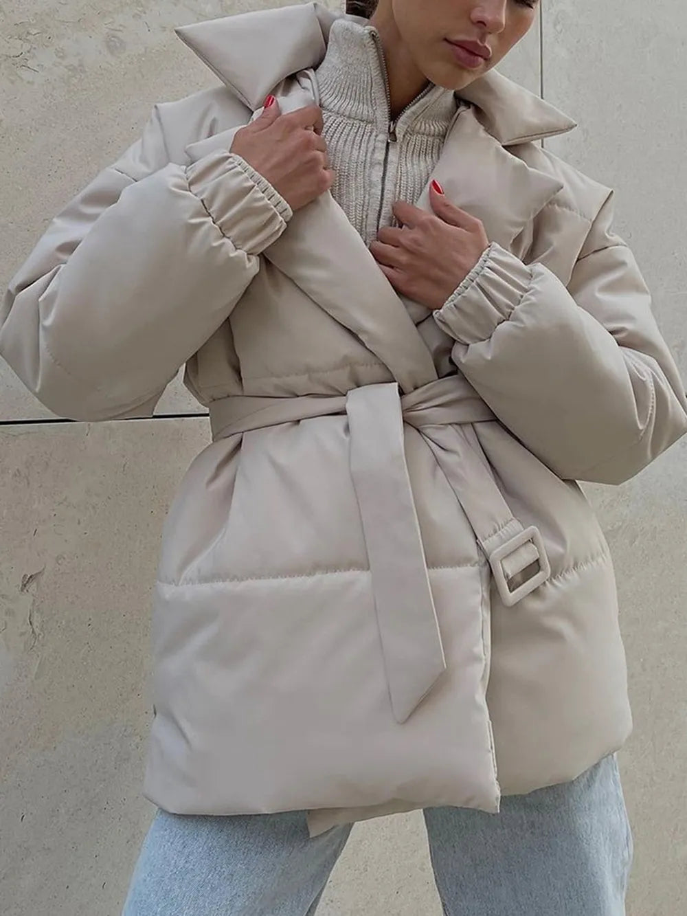 Person wearing a beige puffer coat with a belt against a neutral background
