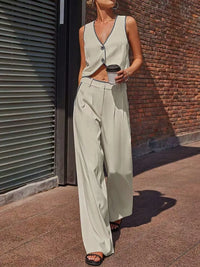 Woman in a light green sleeveless top and wide-leg pants standing against a brick wall.