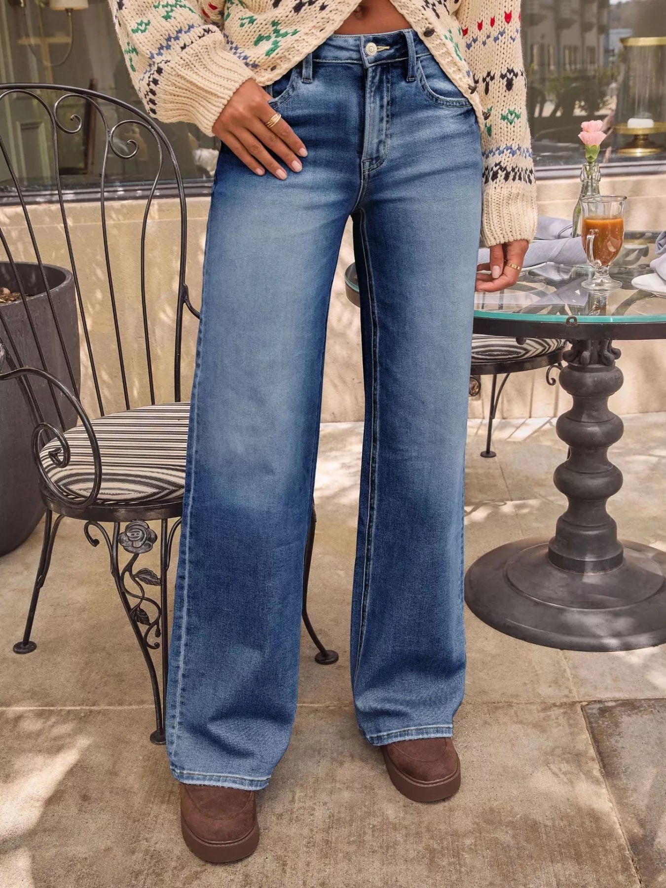 Person wearing blue jeans standing outdoors near a table with a drink.