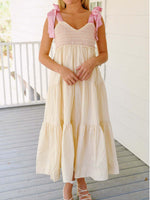 Woman wearing a light-colored dress with pink bow straps on a wooden deck.