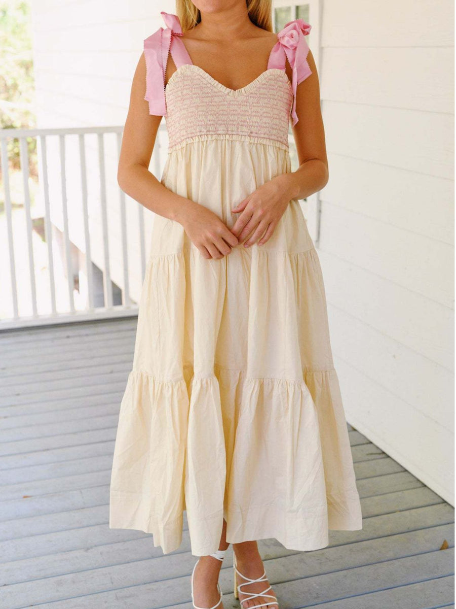 Woman wearing a light-colored dress with pink bow straps on a wooden deck.