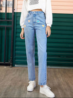Person wearing light blue jeans with heart patches in front of a green door.