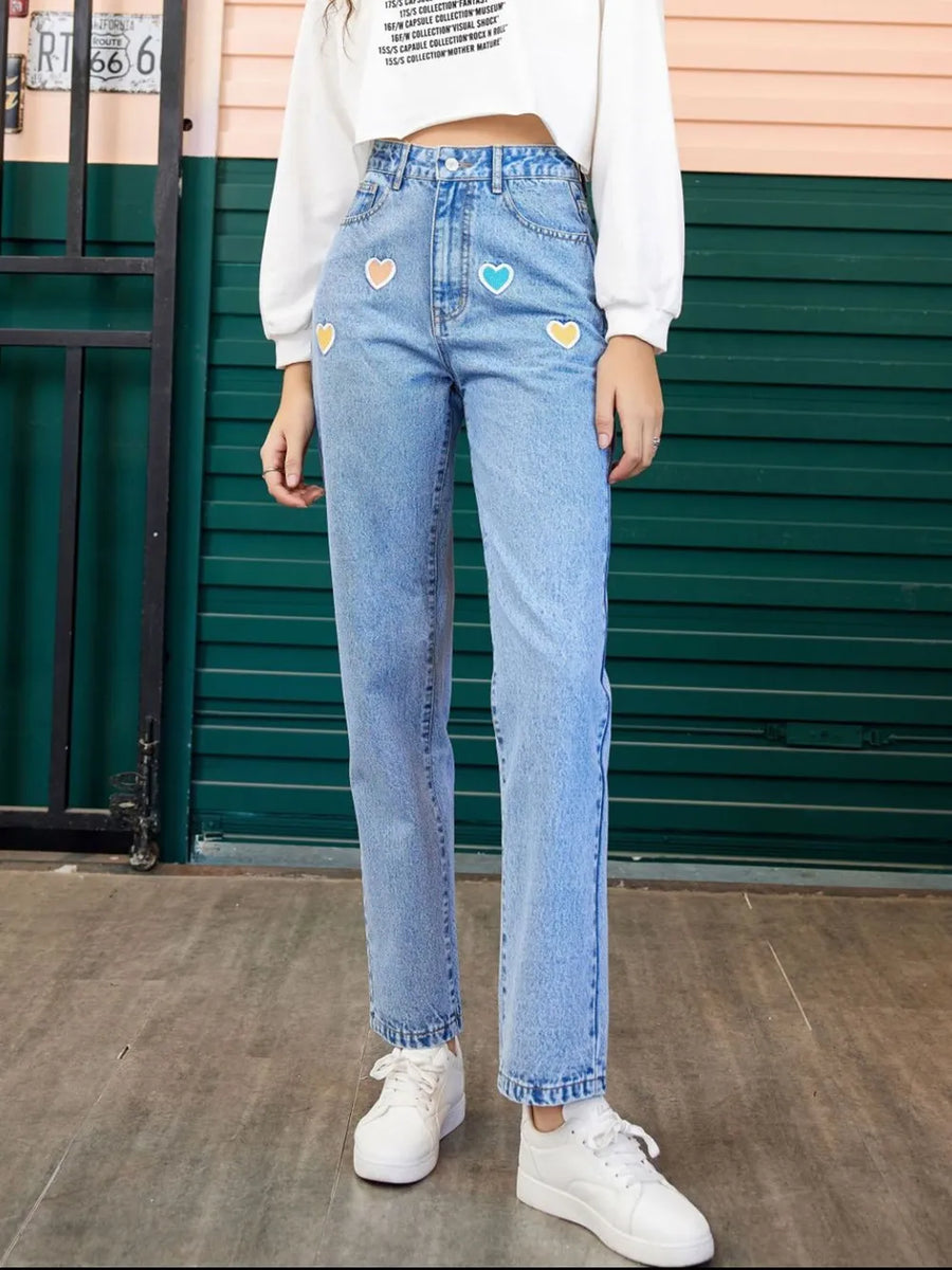 Person wearing light blue jeans with heart patches in front of a green door.
