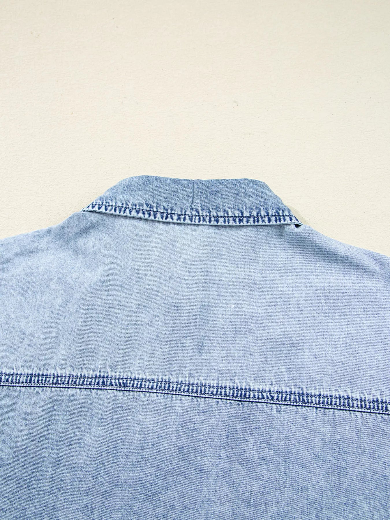 Close-up of a light blue denim shirt on a beige background
