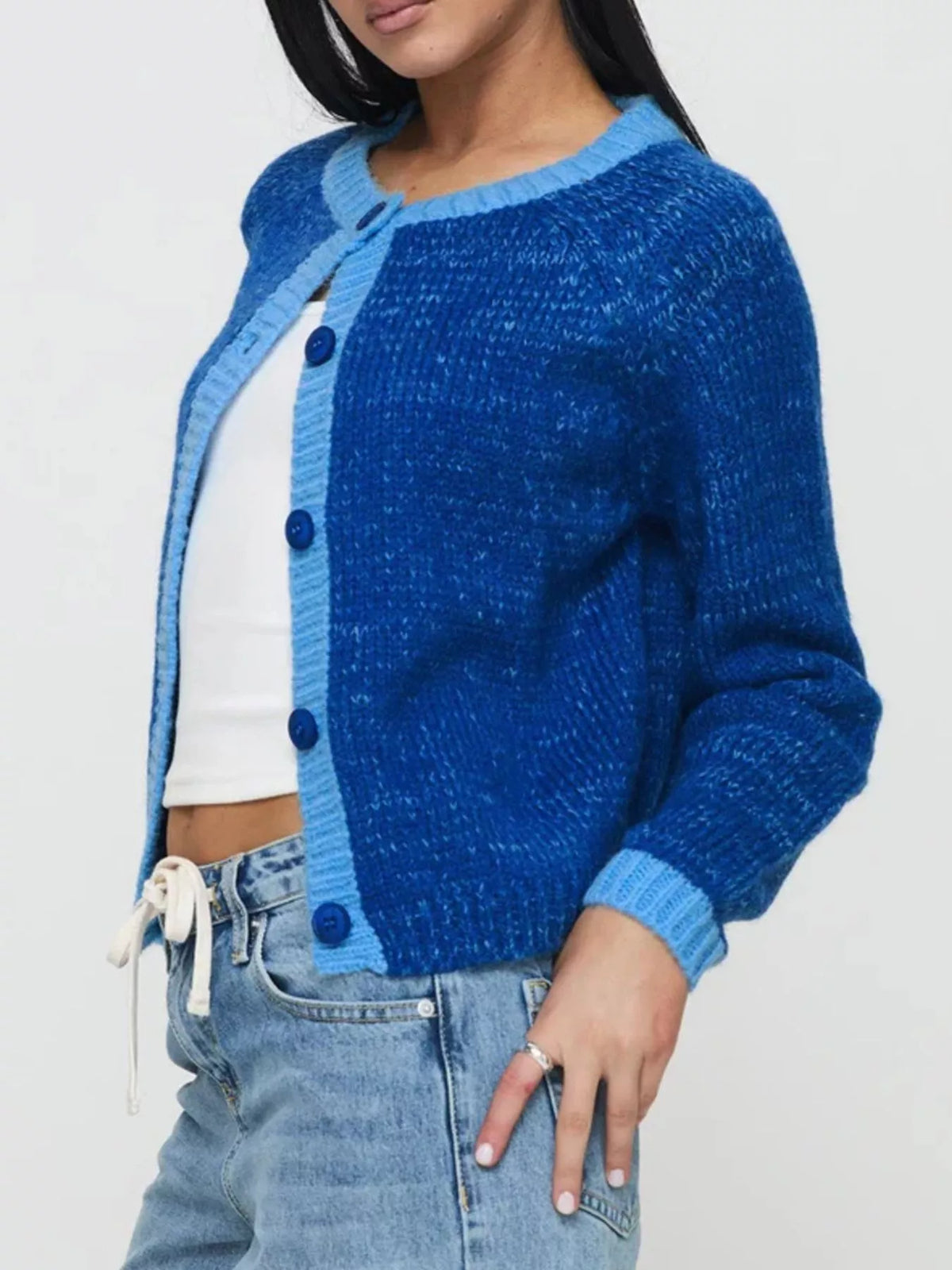 Person wearing a blue cardigan over a white shirt and jeans on a light gray background