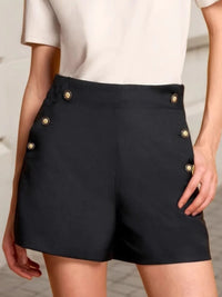 Black shorts with gold buttons worn by a person against a neutral background