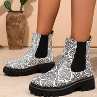 Black and white patterned boots with black soles worn by a person, with a vase and plant in the background.