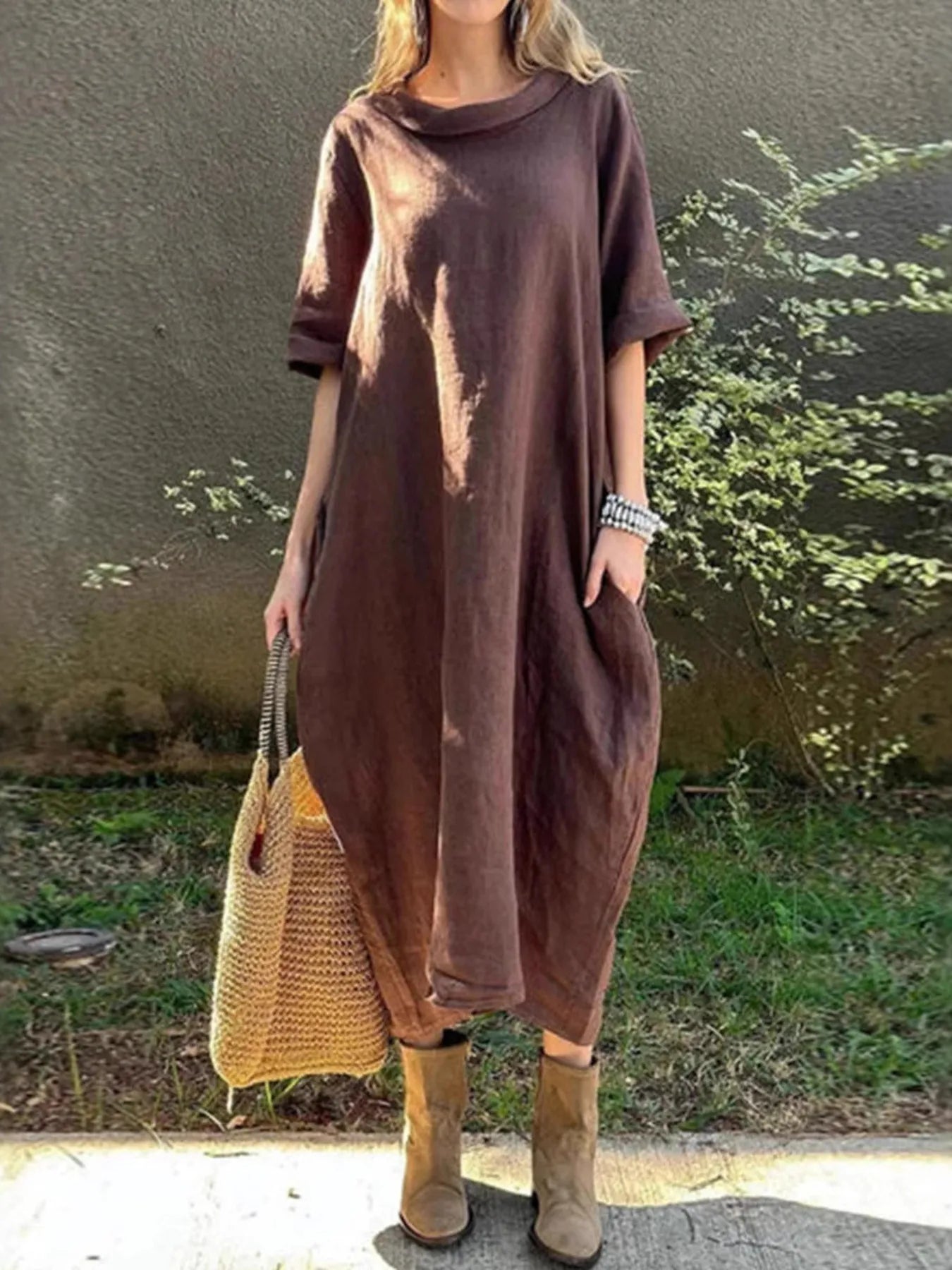 Person wearing a brown dress with a textured bag outdoors.